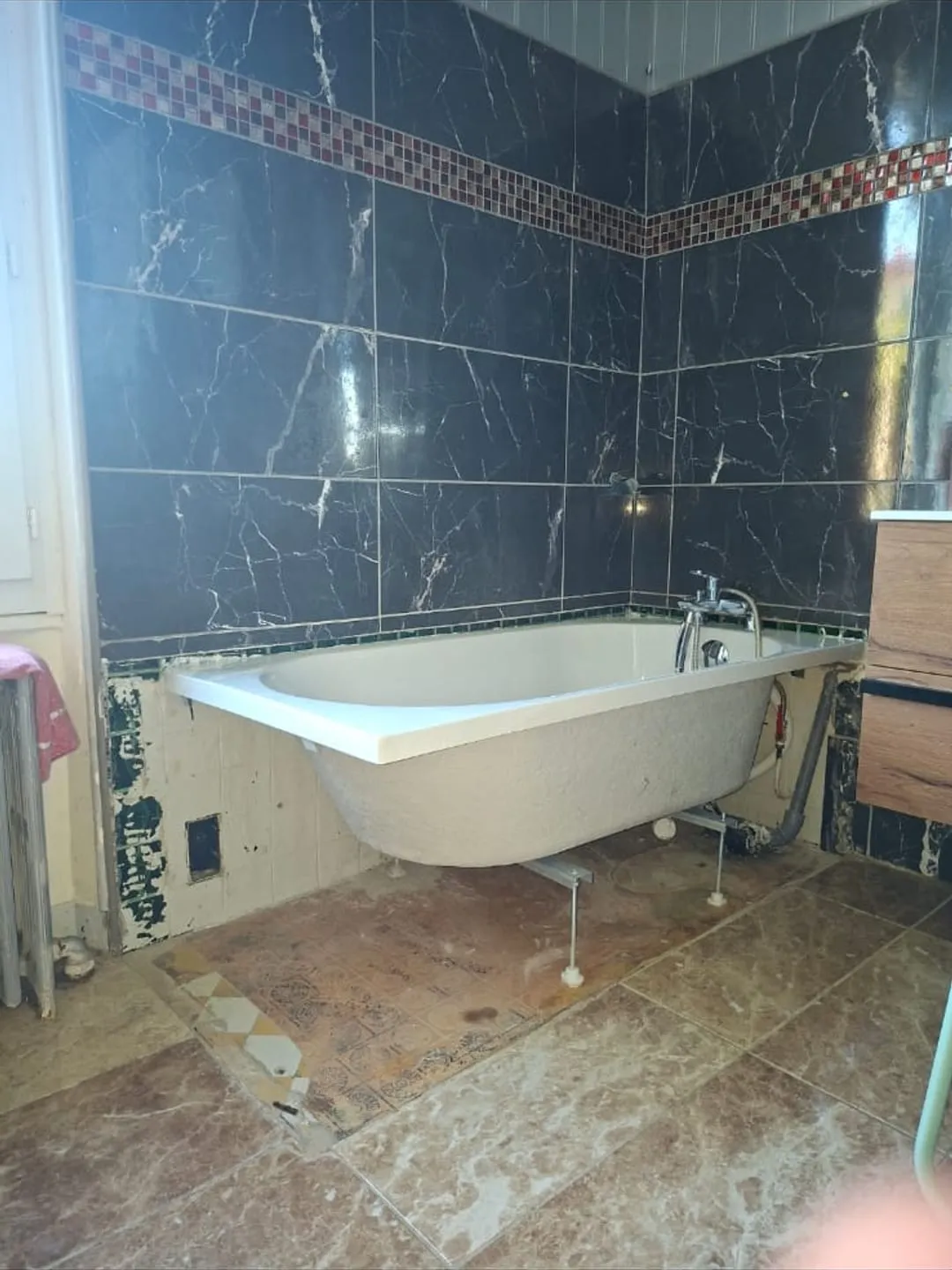 Baignoire au tablier brut et tuyaux apparents avant l'intervention de Bony Plomberie